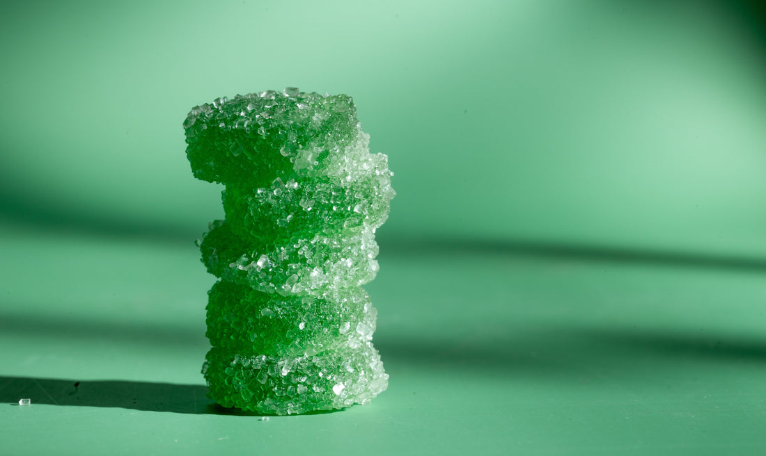 •	Green gummies stacked on top of each other in front of a green background. 
